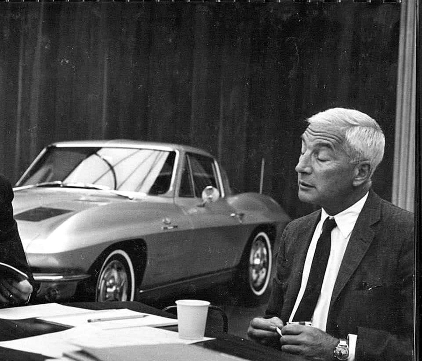 Zora Arkus-Duntov at a desk, a C2 Corvette Sting Ray behind him